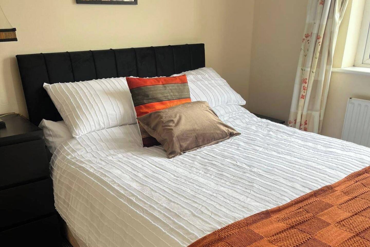 A neatly made bed with a striped bedspread, a black headboard, and two pillows.