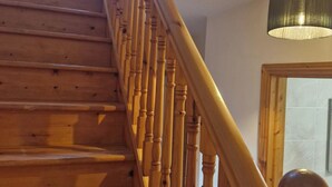 A wooden staircase with a handrail, leading to a room with a tiled wall and a hanging light fixture.