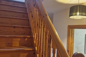 A wooden staircase with a handrail, leading to a room with a tiled wall and a hanging light fixture.