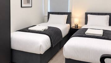 A hotel room with two beds, a wardrobe, a framed picture on the wall, and a window with blinds.