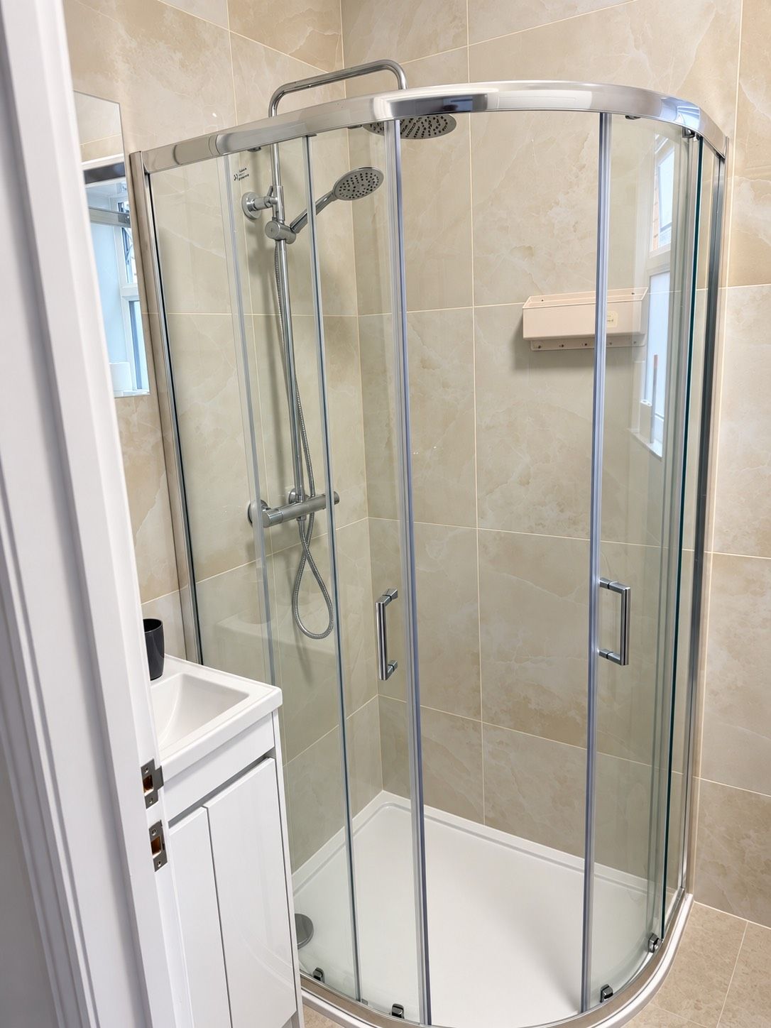 A glass-enclosed shower stall with a handheld showerhead and a wall-mounted showerhead.
