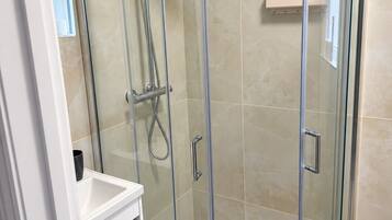 A glass-enclosed shower stall with a handheld showerhead and a wall-mounted showerhead.