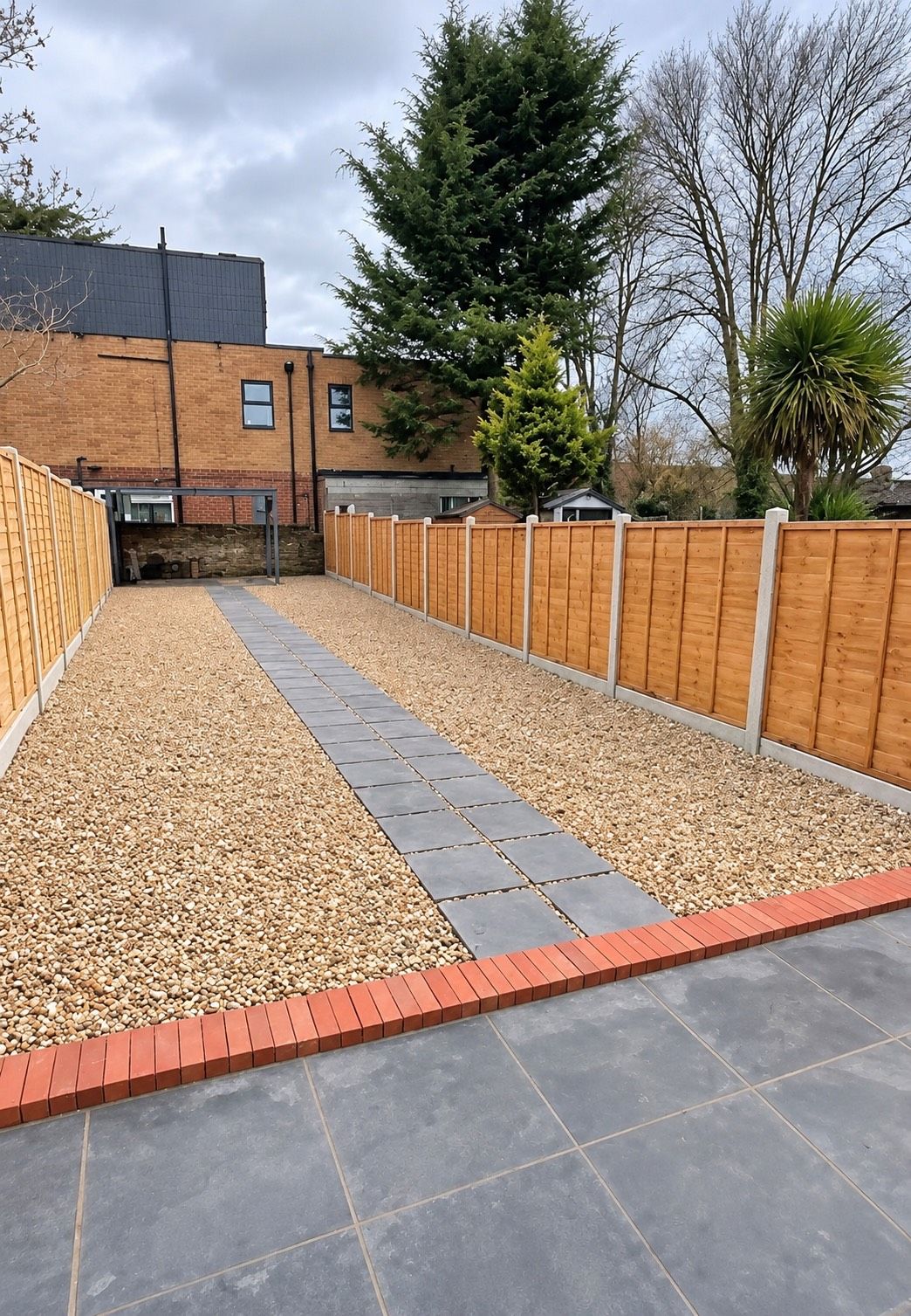A courtyard with a gravel path, wooden fence, and a brick border.