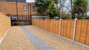 A courtyard with a gravel path, wooden fence, and a brick border.