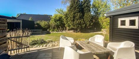 An outdoor patio with a wooden table and white chairs, surrounded by a stone wall and a wooden fence.