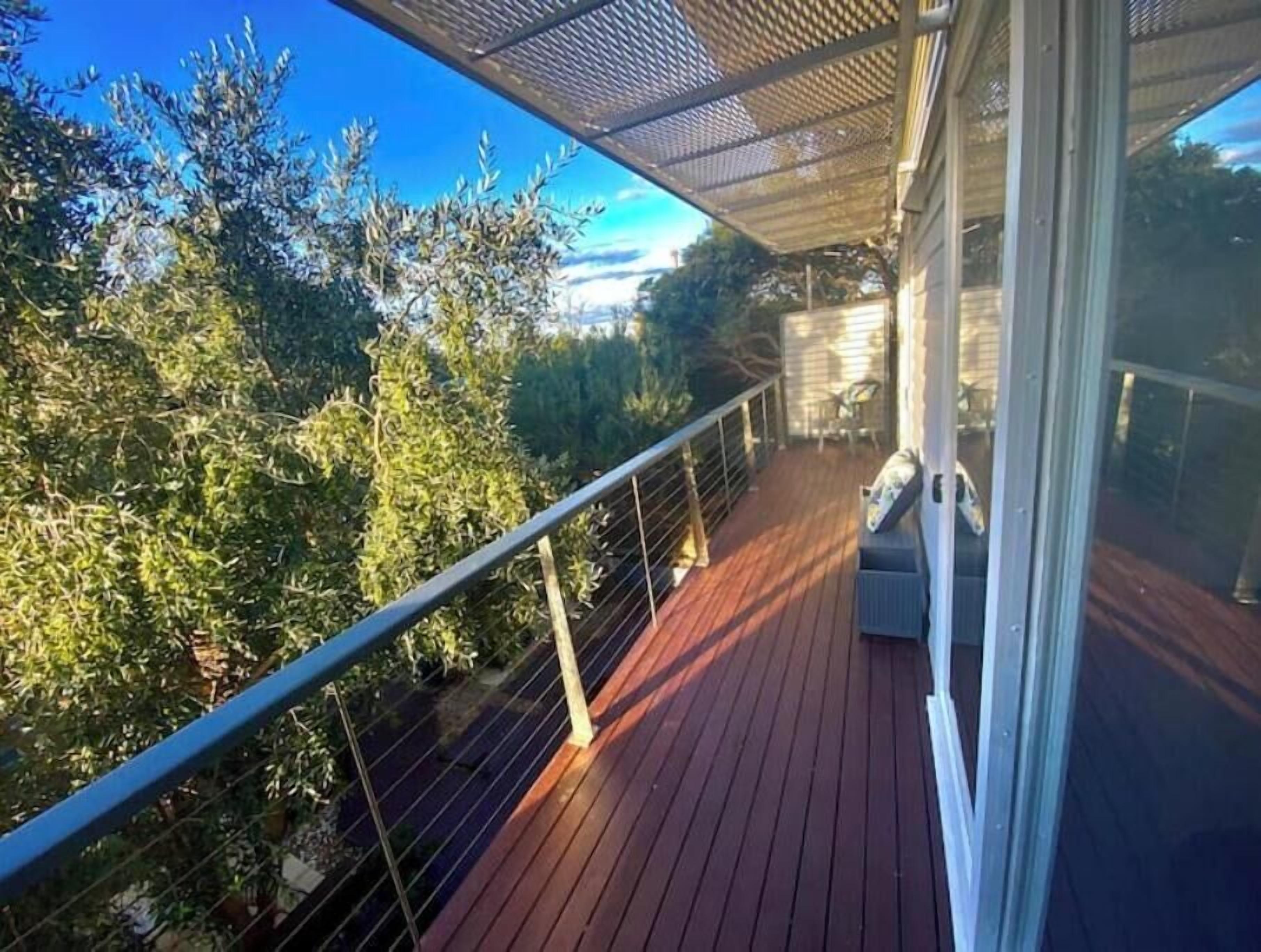 A wooden deck with a metal railing, overlooking a forested area.