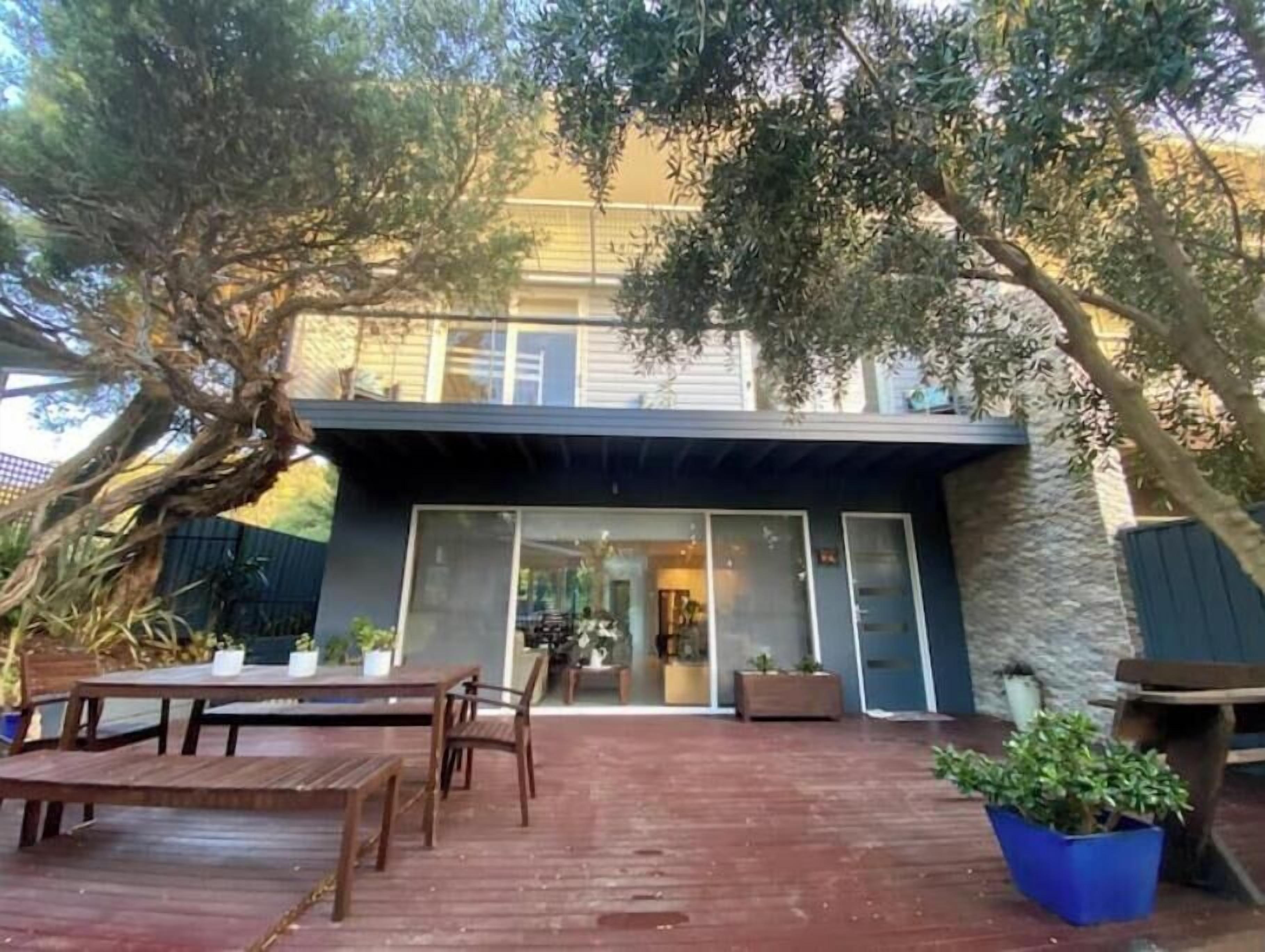 Una casa moderna con un patio que cuenta con una terraza de madera, mobiliario exterior y plantas en macetas.