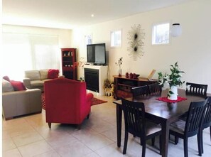 A living room with a red sofa, a dining table with chairs, a television, and a fireplace. - Secluded Sorrento House 800m to Back Beach/Town (Sorrento)
