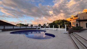 A swimming pool with a curved edge, surrounded by a tiled deck and white lounge chairs.