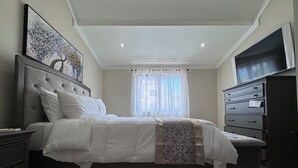 A bedroom with a bed, a dresser, a television, and a window with curtains.