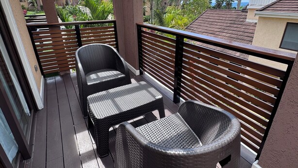 A covered outdoor area with wicker furniture, a wooden deck, and a view of palm trees and buildings.