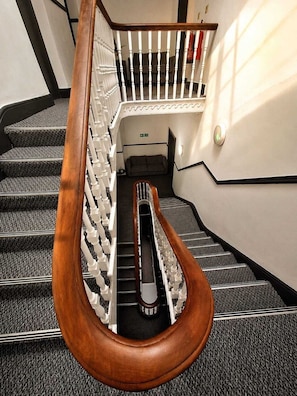 A staircase with a wooden handrail and white balusters, carpeted steps, and a landing area with a door.