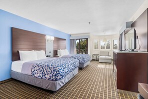 Quarto de hotel com duas camas, uma escrivaninha, uma cadeira, uma televisão e uma janela com persianas.