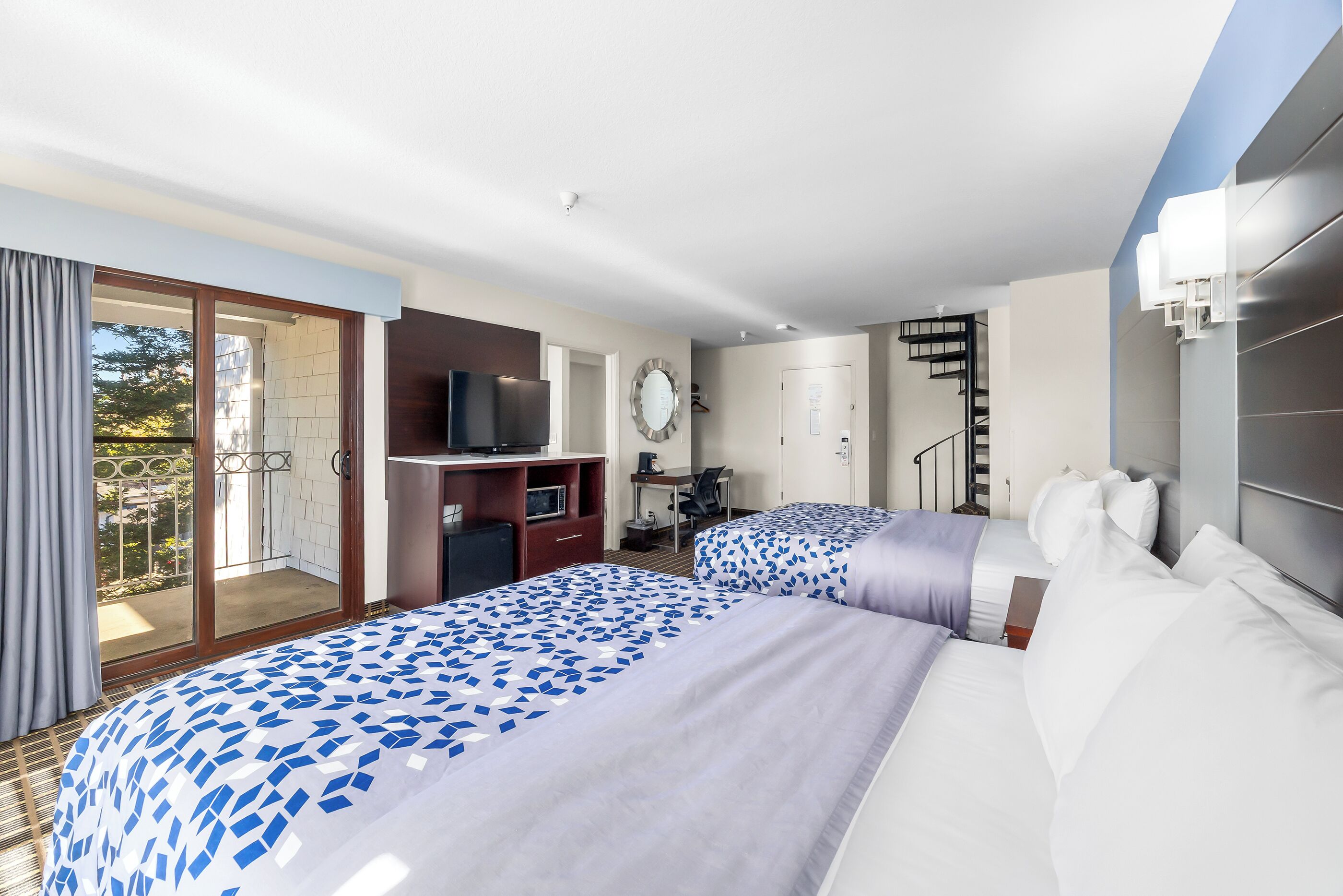 A hotel room with two beds, a desk, a TV, a staircase, and a balcony.
