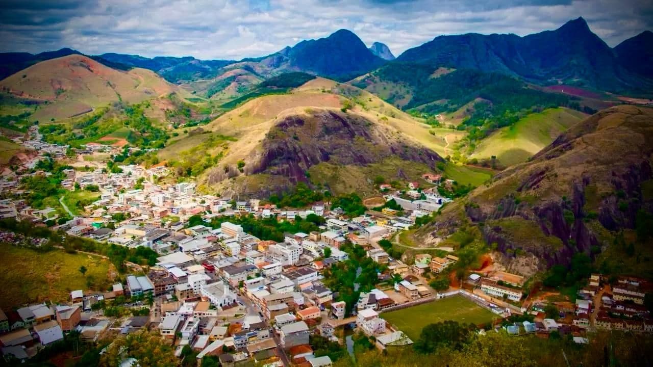 Uma cidade aninhada em um vale, com edifícios residenciais e comerciais, cercada por colinas e montanhas.
