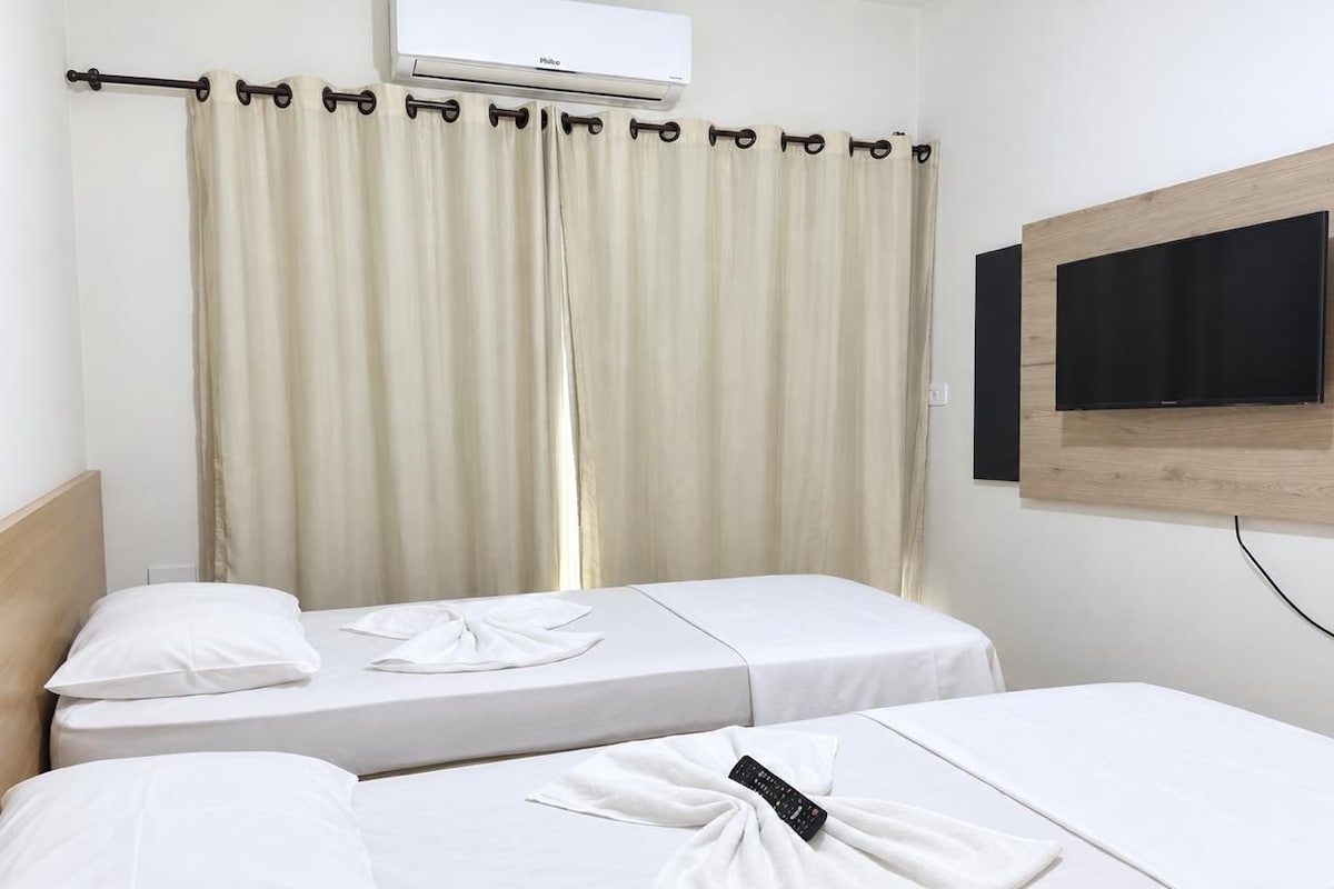 Une chambre d’hôtel avec deux lits, un téléviseur fixé au mur et une fenêtre avec des rideaux.