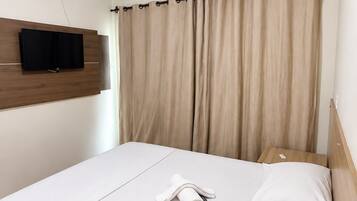 Ett hotellrum med en säng, en platt-TV som är monterad på väggen, en luftkonditioneringsanläggning och en takfläkt.