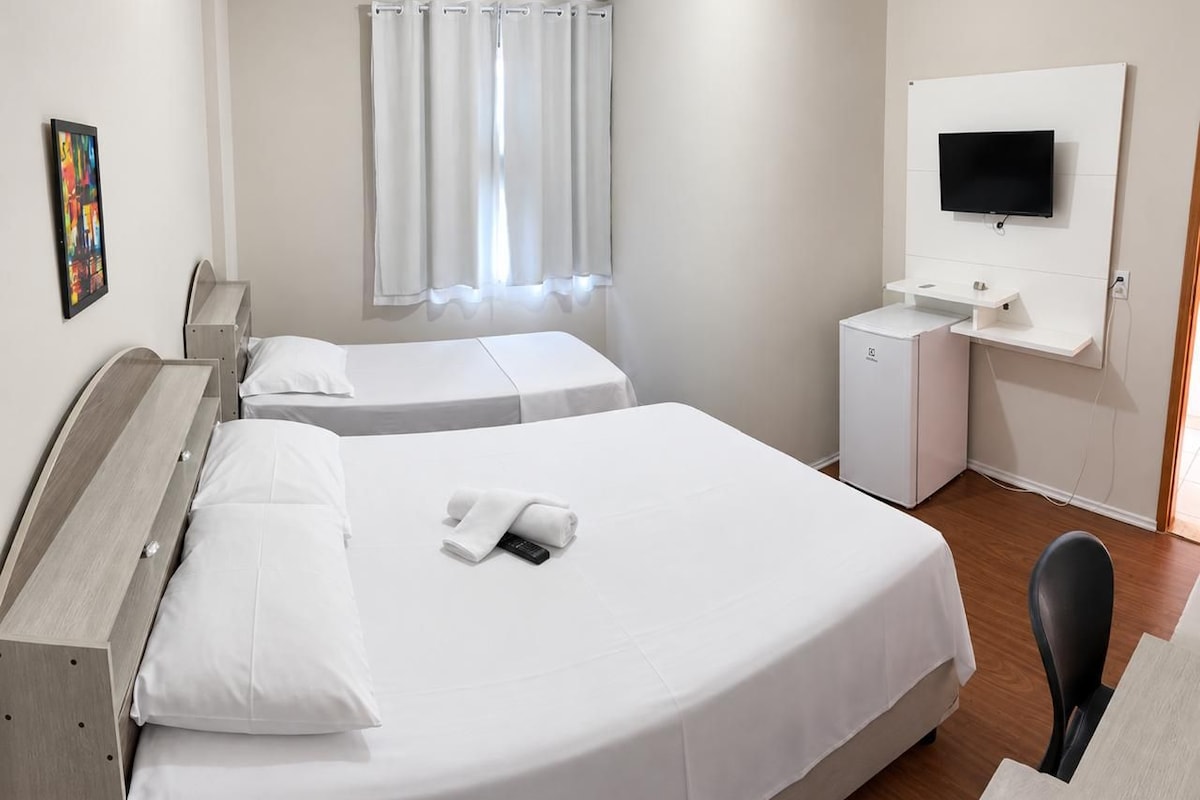 Une chambre d’hôtel avec deux lits, une télévision, un bureau et un petit réfrigérateur.