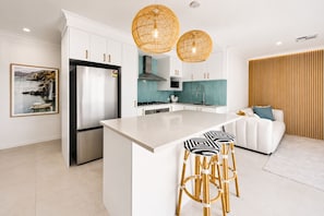A modern kitchen with white cabinetry, a central island, two hanging wicker pendant lights, and a bar stool arrangement. - The Duchess of Duke | Spa, Sauna & Beach Walk (Scarborough)