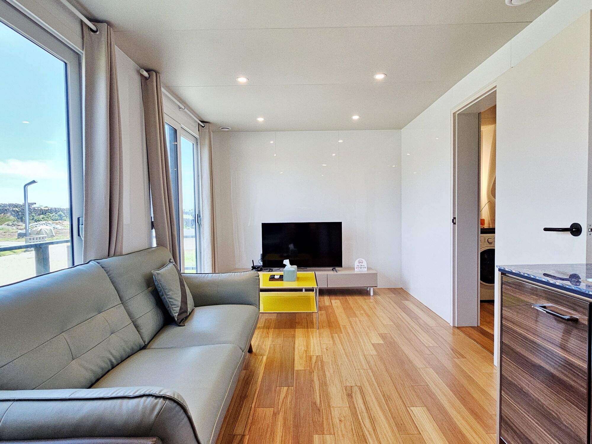 Un salon moderne avec un canapé, un téléviseur et une petite table d’appoint jaune.