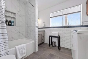 A bathroom with a bathtub, a toilet, a sink, a window, and a towel rack. - Woodland Park Home with Direct Views of Pikes Peak! (Woodland Park)