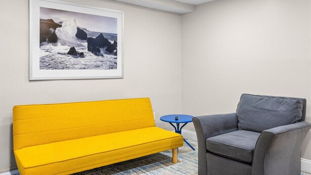 Une pièce avec un canapé jaune, un fauteuil gris, une petite table bleue et une photographie encadrée accrochée au mur.