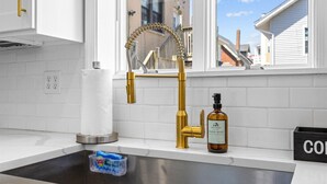 A kitchen with a gold faucet, a paper towel holder, a soap dispenser, and a water filter. - Modern 8BR Ventnor Compound | Patio | BBQ | Games (Ventnor City)