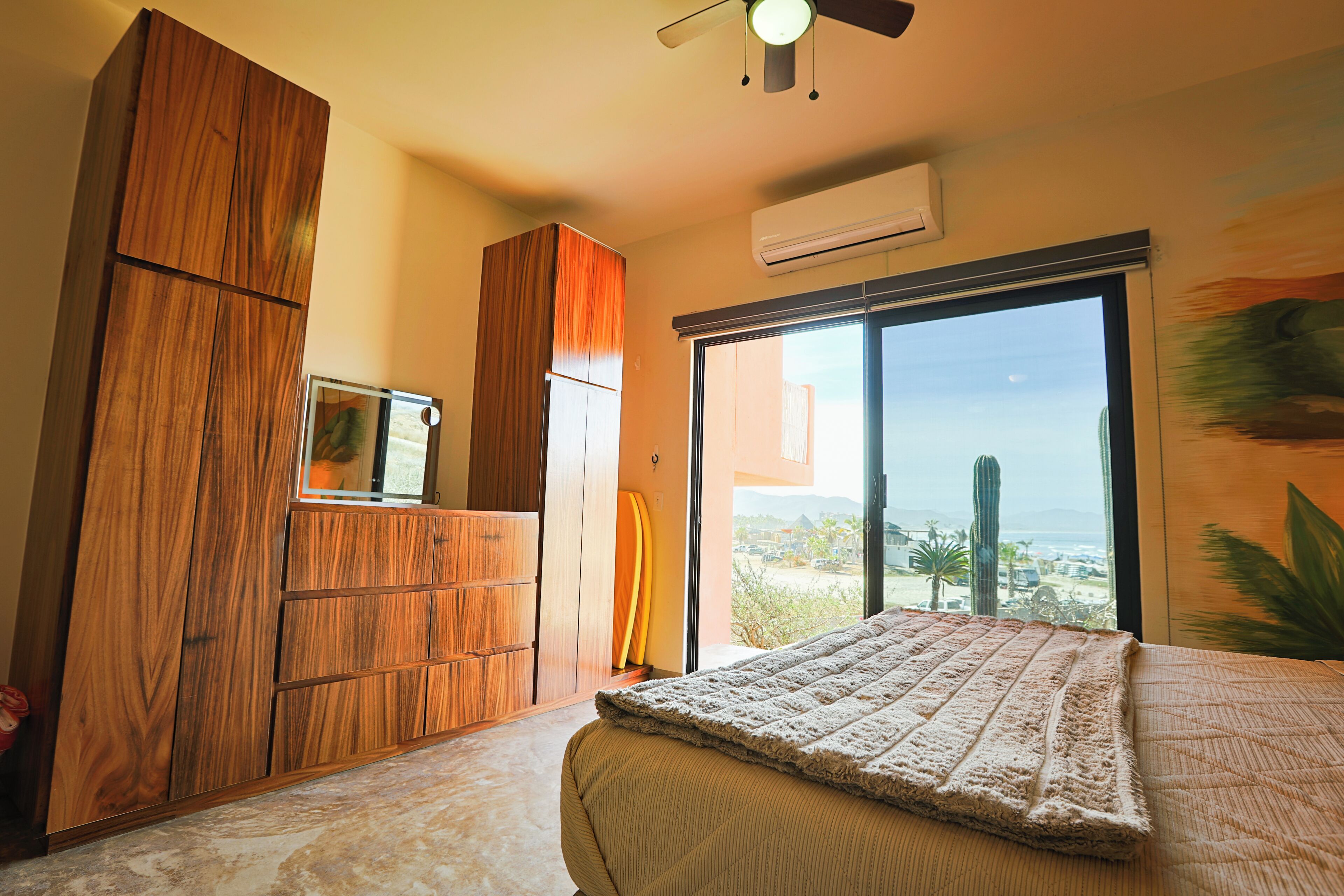A bedroom with a large window, a ceiling fan, and a wooden wardrobe.