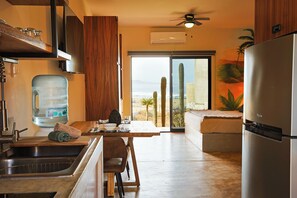 Eine Küche mit Wasserspender, Kühlschrank, Esstisch und Stühlen sowie Blick ins Freie.