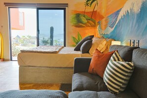Ein Zimmer mit einem Bett, einer Couch, Blick durch eine Schiebetür und Wandgemälde.