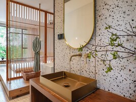 Un baño con un lavamanos rectangular, un separador de madera, un espejo y una pared de terrazo.