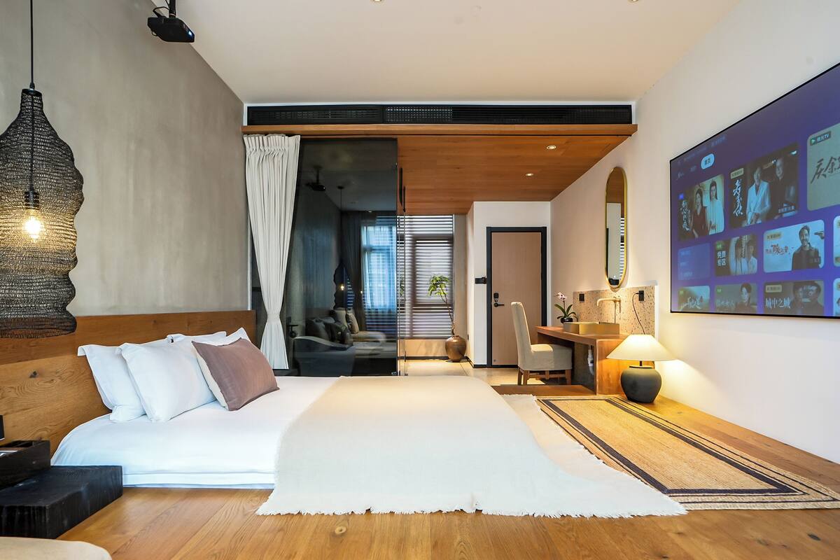 Ett modernt hotellrum med en stor säng, ett skrivbord, en stol, en tv-skärm och ett stort fönster.