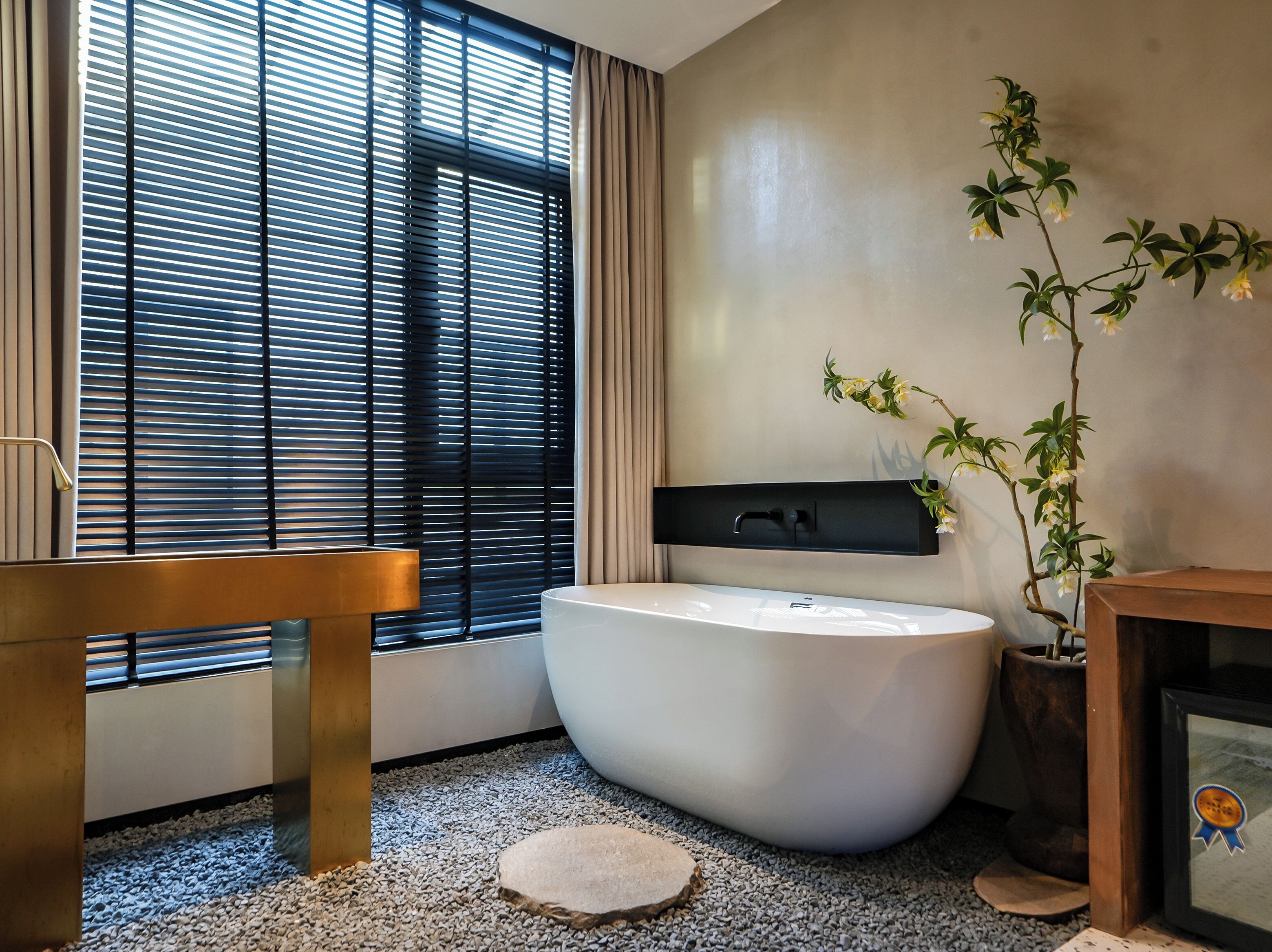 A modern bathroom with a freestanding bathtub, a wooden bench, and a potted plant.