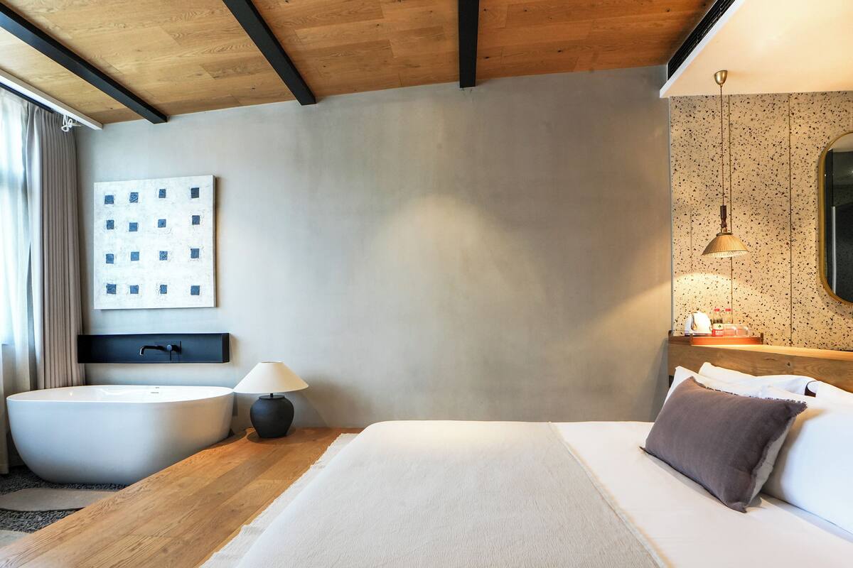 Ett modernt hotellrum med ett stort badkar, en säng med en kudde, ett sängbord med en lampa och en väggmonterad TV.