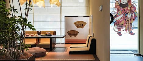 Un interior japonés tradicional con suelo de tatami, una mesa baja con cojines, faroles de papel colgantes y una gran obra de arte enmarcada en la pared.