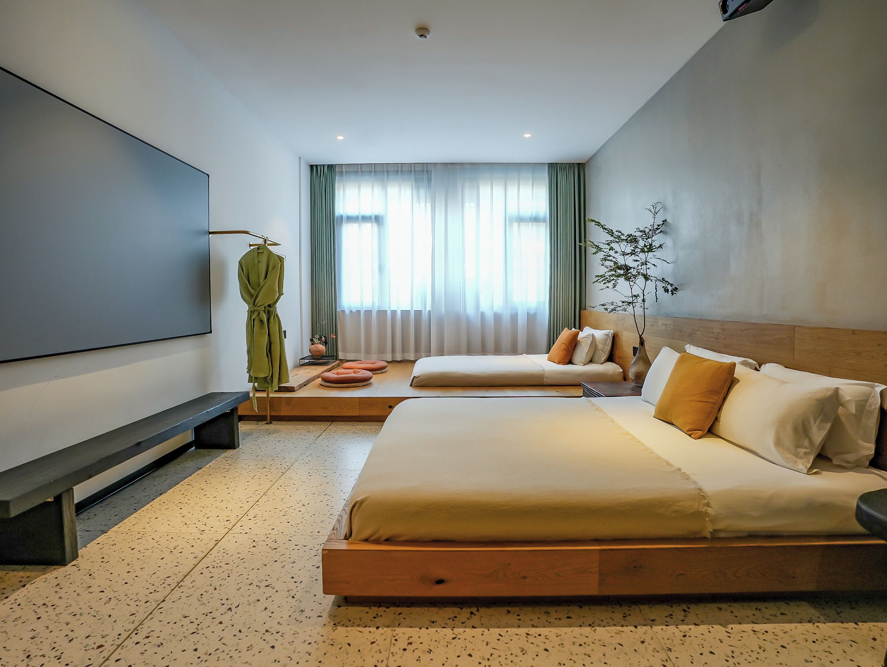 A modern hotel room with a large bed, a television, a seating area with cushions, and a window with curtains.