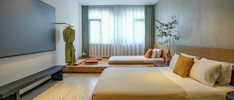 A modern hotel room with a large bed, a television, a seating area with cushions, and a window with curtains.
