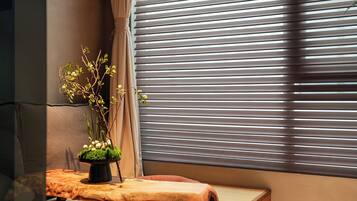 A room with a bed, a potted plant, and a window with blinds.