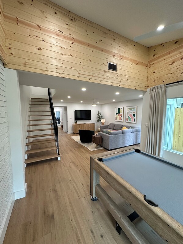 Ein Holzinnenraum mit Billardtisch, einer Couch, einem Fernseher und einer Treppe.