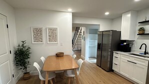 Une cuisine moderne avec des meubles blancs, un réfrigérateur en acier inoxydable et une table à manger en bois, accompagnée de chaises.