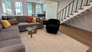 Un salon moderne avec un canapé, un fauteuil, une table basse en verre et un escalier.