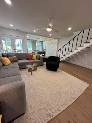 Ein stilvolles Wohnzimmer mit Sofa, Sessel, Glastisch und einer Treppe.