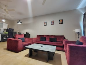 Una sala de estar con un sofá rojo, una mesa de centro, un ventilador de techo y un televisor instalado en la pared.