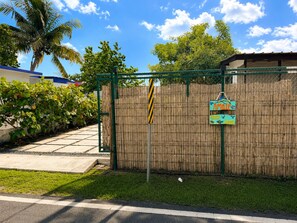 Ein von einer Hecke umschlossener Bereich mit einer Bambuswand, einer Palme und einem Schild, das ein Strandhaus kennzeichnet.