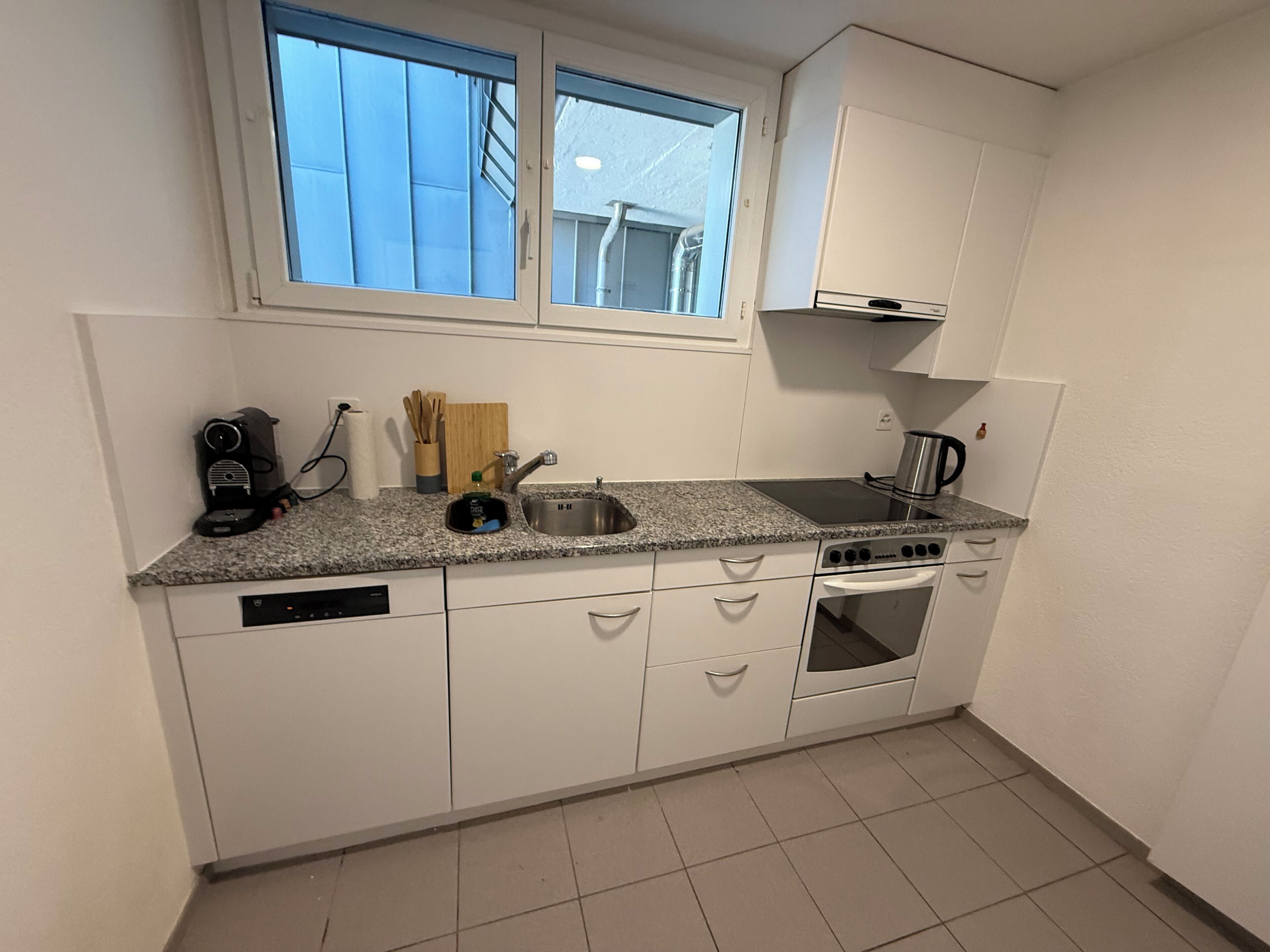 A compact kitchen with a dishwasher, stove, and a window above the sink.