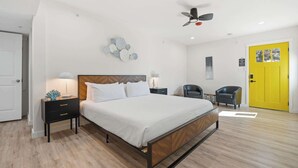 Ein Schlafzimmer mit Bett, Nachttischen, einem Sessel, einem Deckenventilator und einer gelben Tür.