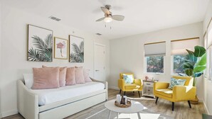 A modern living room with a white sofa, yellow armchairs, a ceiling fan, and large windows. - 2BR Coastal Suite Walk to McGee Beach (Corpus Christi)