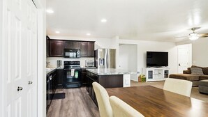 A modern kitchen with dark cabinetry, a central island, and a dining area with a wooden table and chairs. - 5 BR Family Fun, Sleep 12, Climbing Wall & Games (Meridian)