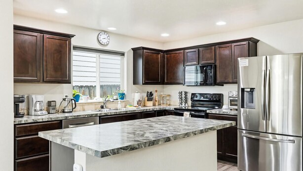 A modern kitchen with dark wood cabinets, stainless steel appliances, a marble island, and a window with blinds. - 5 BR Family Fun, Sleep 12, Climbing Wall & Games (Meridian)