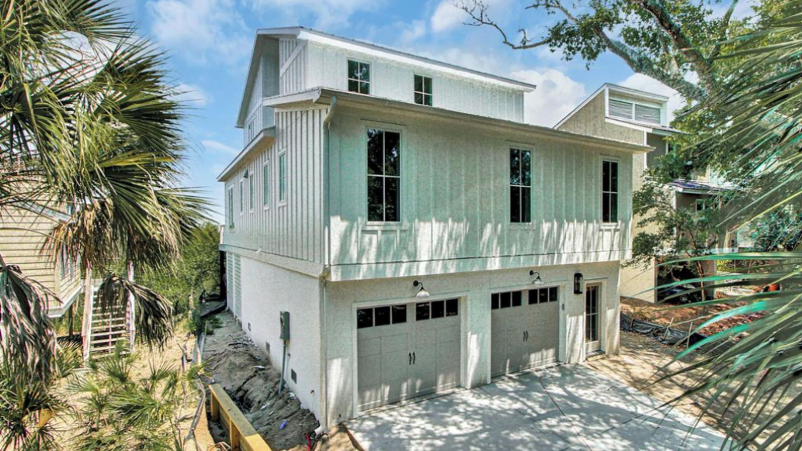 A two-story house with a garage, surrounded by palm trees.